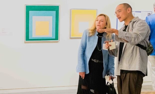 Two people looking at art, two Albers paintings behind them.